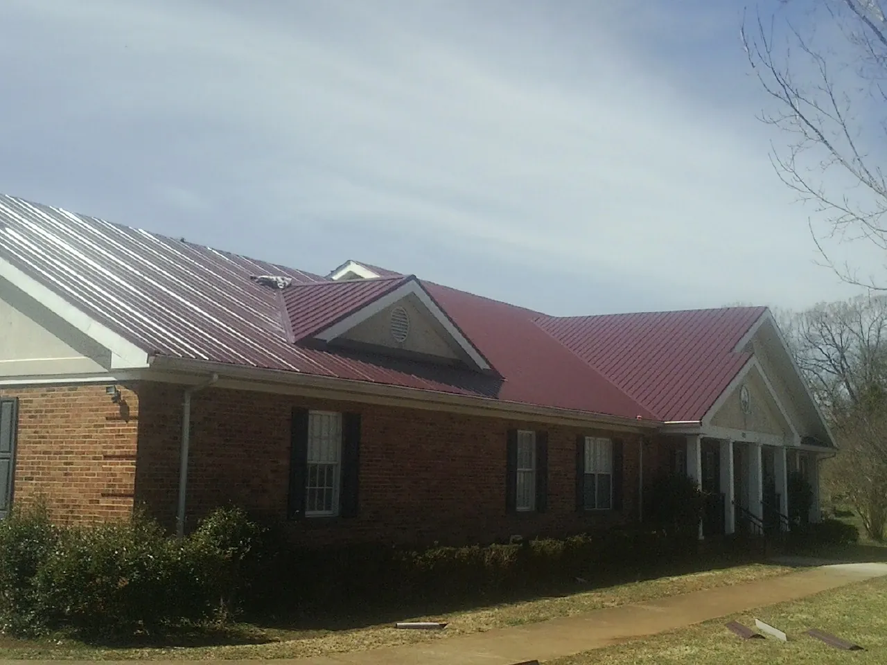Red metal roof with gabled entries on a long brick building, from a Hail Damage Roof Repair job in North Brookfield