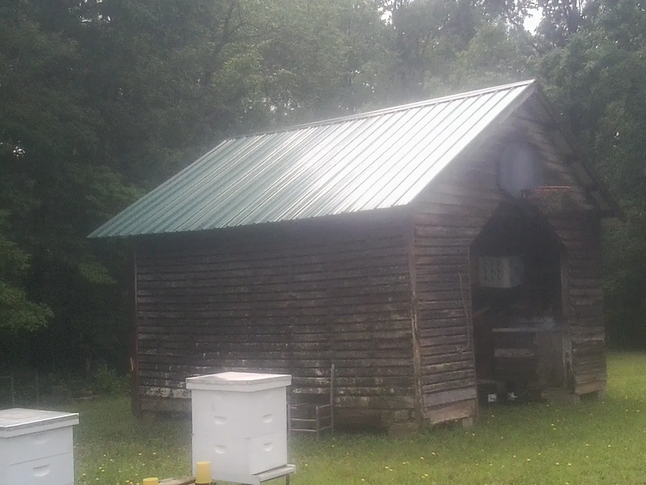 Green metal roof on a weathered barn beside stacked beehives in North Brookfield