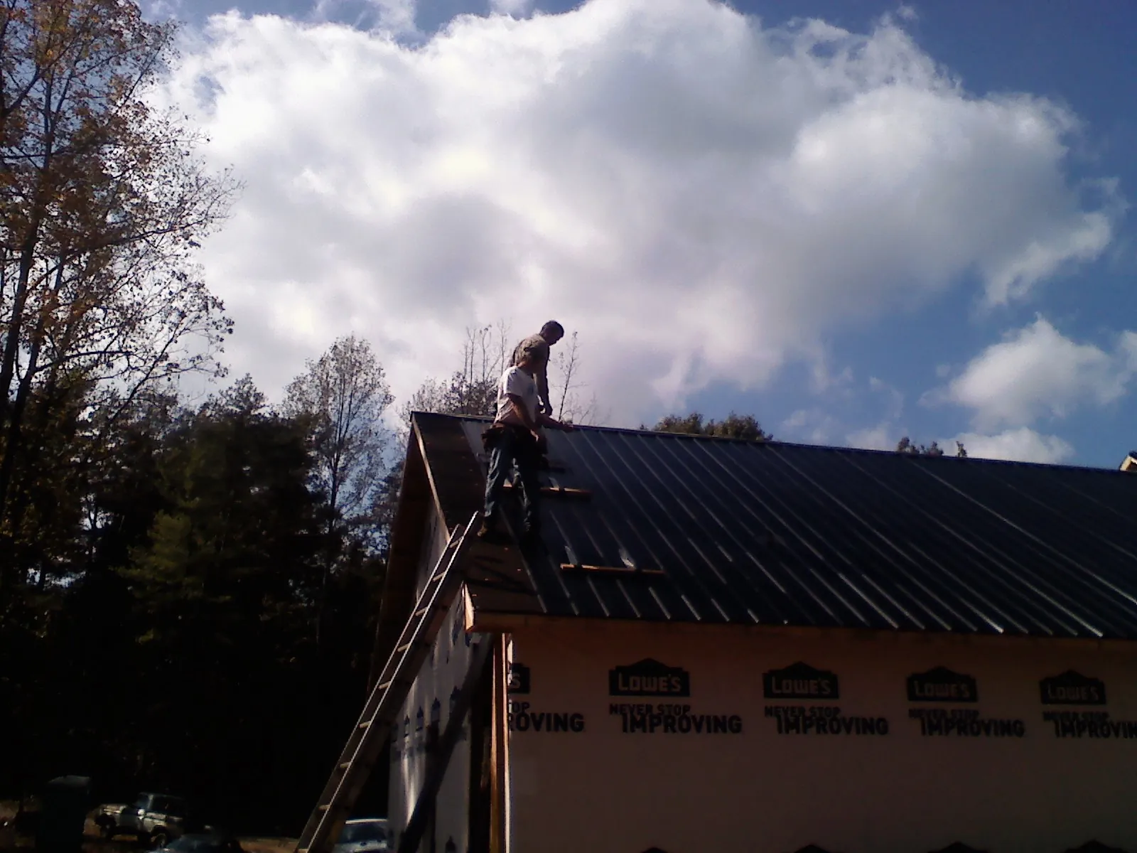 Roofer fastening dark metal panels high against a cloudy sky, from a Roof Inspection job in North Brookfield