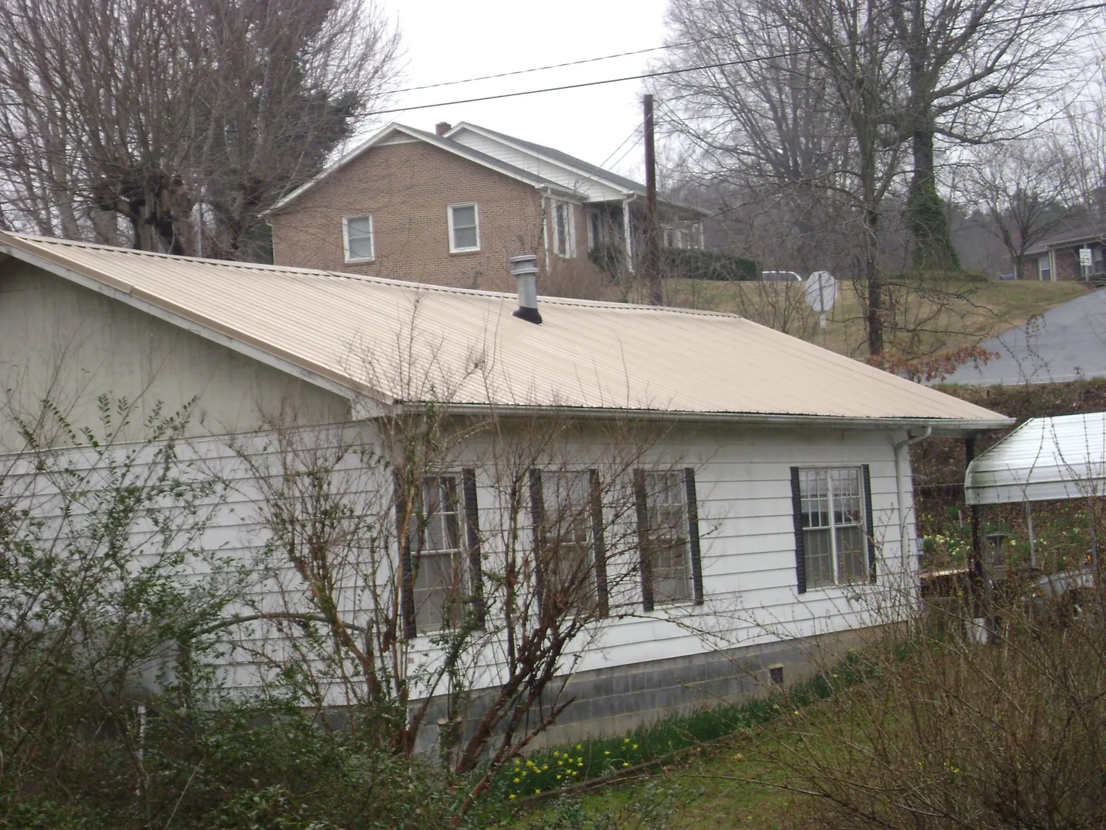 Tan metal roof on a white sided house set into a hillside — Commercial Roofing by Roofing Brothers in North Brookfield