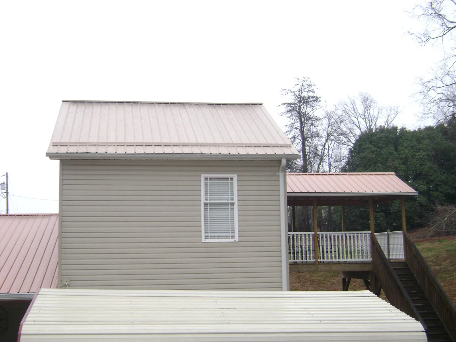 Tan metal roofs on a two story addition and attached porch, from a Roof Replacement job in North Brookfield
